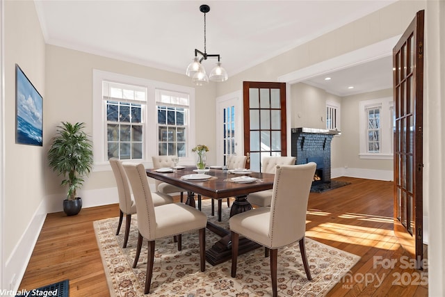 dining area featuring baseboards, ornamental molding, hardwood / wood-style flooring, a brick fireplace, and a chandelier