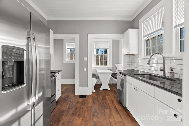 kitchen with dark wood-style floors, dark stone counters, a sink, white cabinets, and appliances with stainless steel finishes