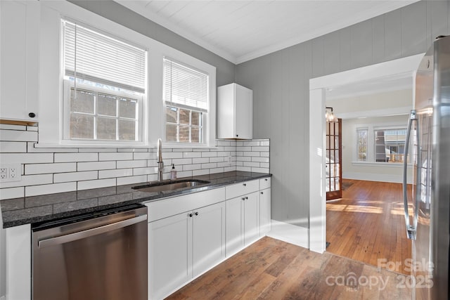 kitchen with dark stone counters, decorative backsplash, hardwood / wood-style flooring, stainless steel appliances, and a sink