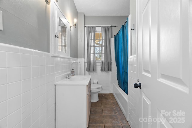 full bathroom with a wainscoted wall, toilet, vanity, shower / tub combo, and tile walls