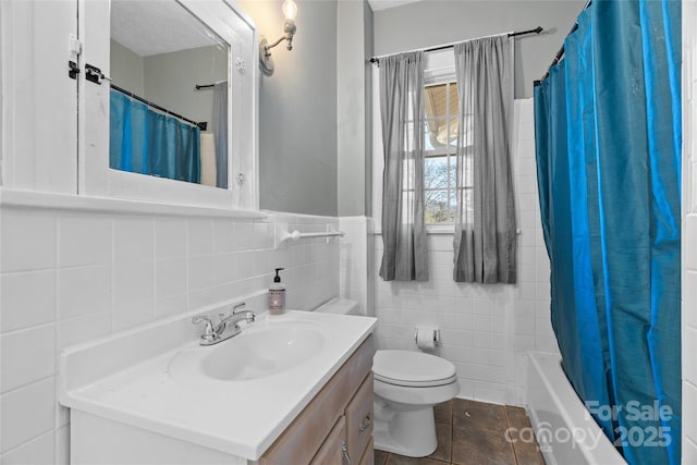 full bathroom with a wainscoted wall, toilet, vanity, tile patterned floors, and tile walls