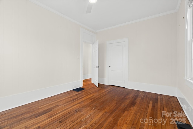 empty room with dark wood-style floors, visible vents, crown molding, and baseboards