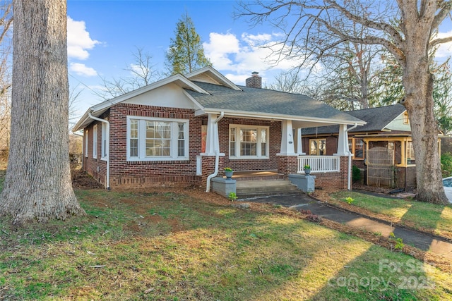 view of front facade featuring a porch, roof with shingles, a front yard, brick siding, and a chimney