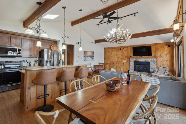 dining space featuring high vaulted ceiling, a fireplace, wood-type flooring, beamed ceiling, and a chandelier