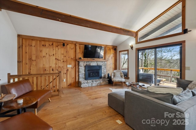 living area featuring wooden walls, a stone fireplace, vaulted ceiling with beams, and light wood finished floors