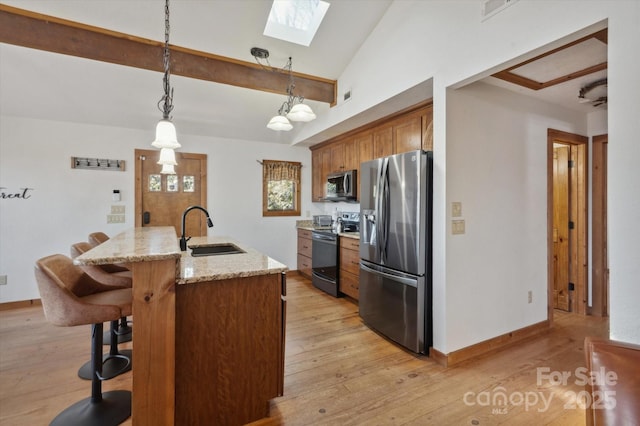 kitchen featuring a sink, stainless steel appliances, light wood-style floors, lofted ceiling with skylight, and a kitchen breakfast bar