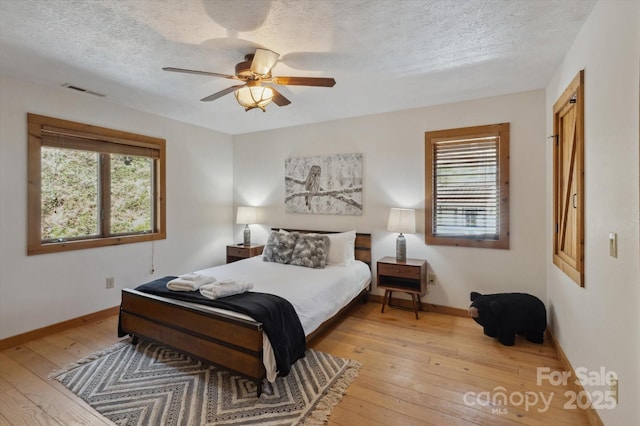 bedroom with multiple windows, light wood-style floors, and a textured ceiling