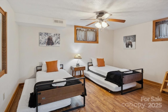 bedroom with visible vents, baseboards, wood finished floors, and a ceiling fan