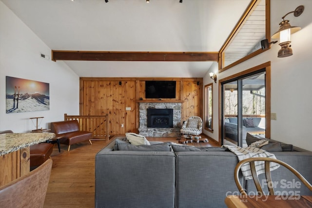 living area featuring beamed ceiling, high vaulted ceiling, wood finished floors, wooden walls, and a fireplace