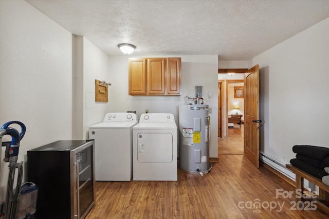 laundry room with electric water heater, light wood-type flooring, washer and dryer, cabinet space, and a textured ceiling