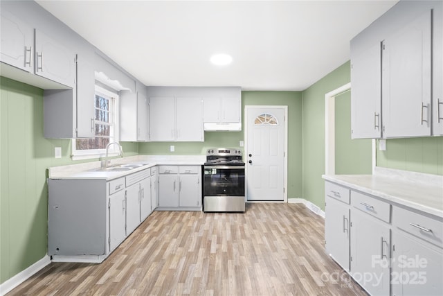 kitchen featuring a sink, under cabinet range hood, light countertops, and stainless steel range with electric cooktop