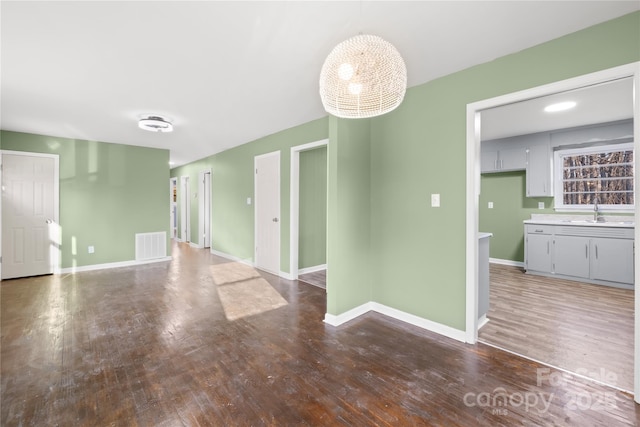 empty room featuring wood finished floors, visible vents, baseboards, a sink, and a chandelier