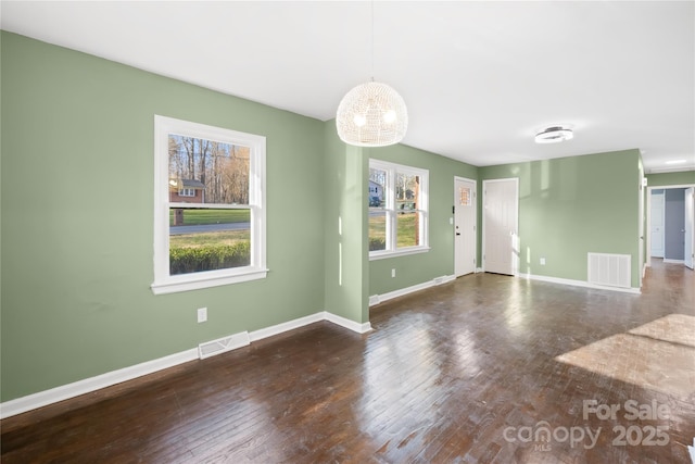 unfurnished living room with hardwood / wood-style floors, baseboards, visible vents, and a chandelier