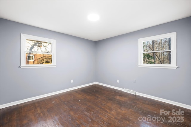 unfurnished room featuring visible vents, baseboards, a healthy amount of sunlight, and dark wood finished floors