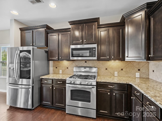 kitchen featuring light stone counters, dark wood-style flooring, decorative backsplash, dark brown cabinets, and appliances with stainless steel finishes