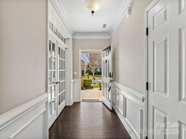 entryway with ornamental molding, dark wood finished floors, french doors, wainscoting, and a decorative wall