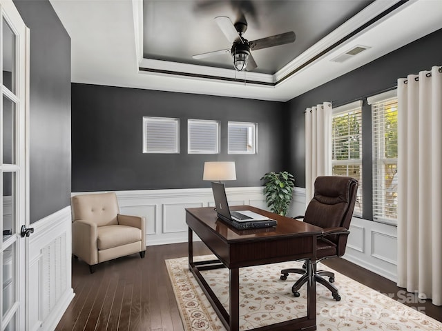 office space with visible vents, a wainscoted wall, dark wood-type flooring, a raised ceiling, and ceiling fan