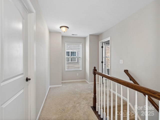 hallway featuring an upstairs landing, visible vents, baseboards, and carpet floors