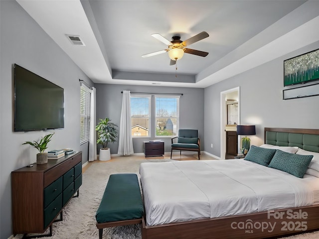 bedroom with visible vents, baseboards, light carpet, ensuite bathroom, and a raised ceiling