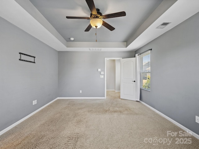 spare room with carpet, baseboards, visible vents, a tray ceiling, and ceiling fan