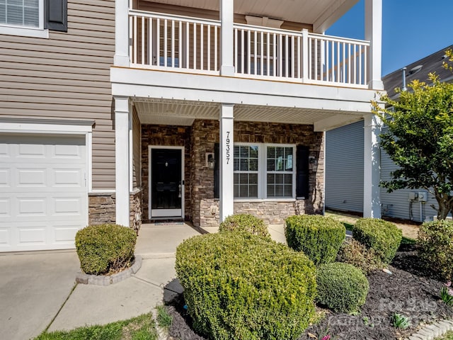 entrance to property featuring a porch, a balcony, a garage, and stone siding