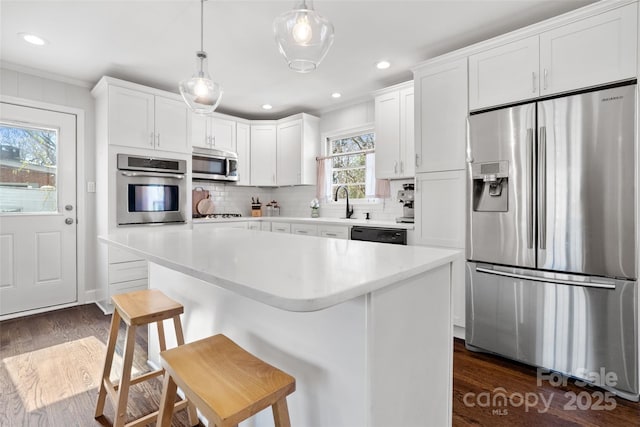 kitchen with a breakfast bar area, stainless steel appliances, decorative backsplash, dark wood-type flooring, and white cabinets