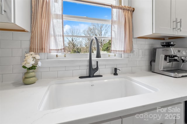 details with a sink, tasteful backsplash, and white cabinetry