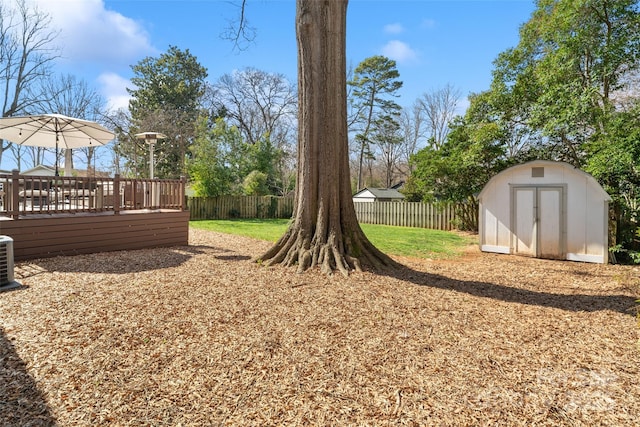 view of yard featuring an outbuilding, cooling unit, a wooden deck, a fenced backyard, and a storage unit