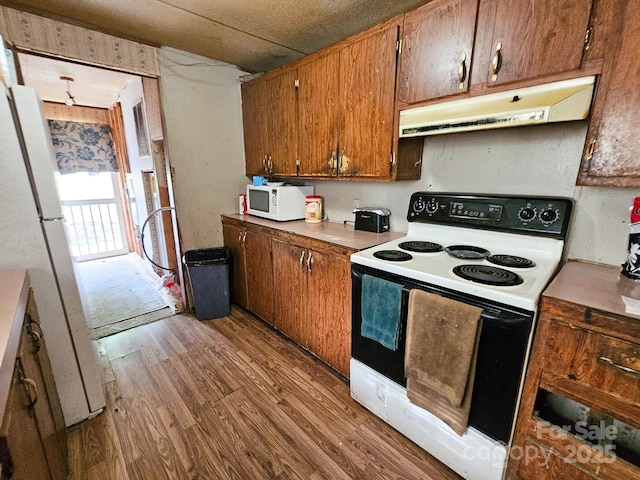 kitchen featuring brown cabinets, light countertops, under cabinet range hood, wood finished floors, and white appliances