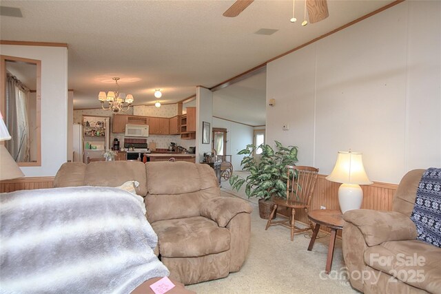 living room featuring visible vents, lofted ceiling, ornamental molding, ceiling fan with notable chandelier, and light colored carpet