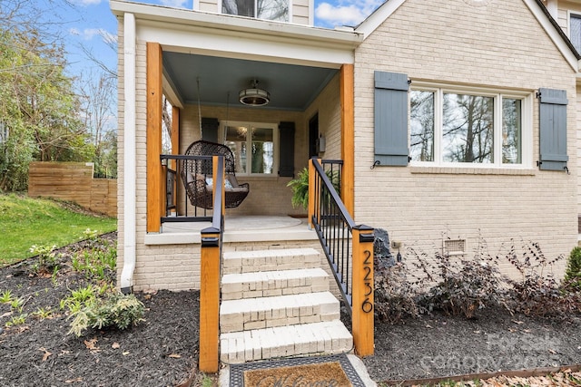 entrance to property with brick siding, crawl space, a porch, and fence