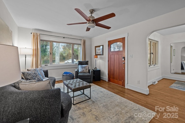 living room featuring ceiling fan, baseboards, arched walkways, and wood finished floors