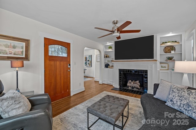 living area with built in shelves, wood finished floors, baseboards, arched walkways, and a tile fireplace