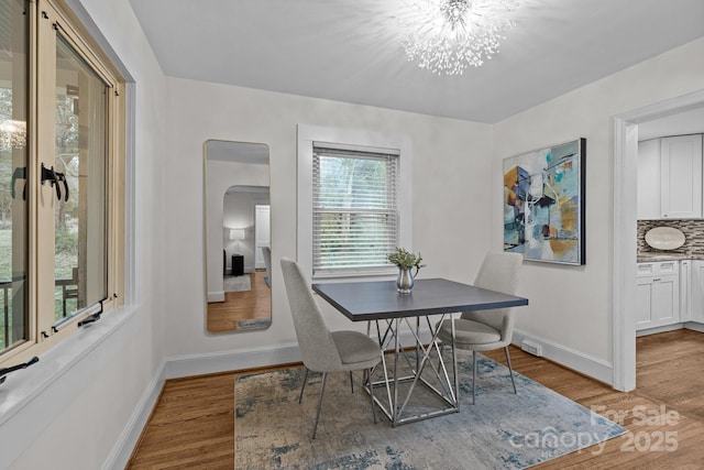 dining space with baseboards, arched walkways, an inviting chandelier, and wood finished floors