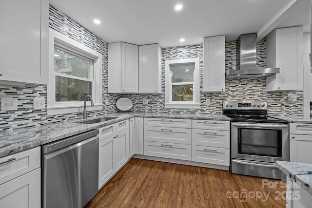 kitchen with appliances with stainless steel finishes, white cabinetry, wall chimney exhaust hood, and a sink