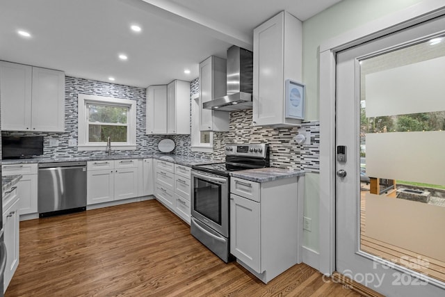 kitchen featuring light stone countertops, wood finished floors, a sink, appliances with stainless steel finishes, and wall chimney exhaust hood