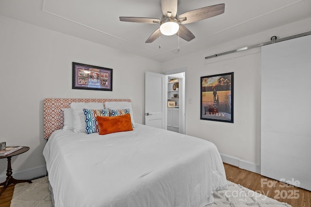 bedroom featuring ceiling fan, baseboards, a barn door, and wood finished floors