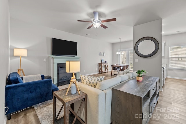 living area with ceiling fan, baseboards, light wood-style floors, and a glass covered fireplace