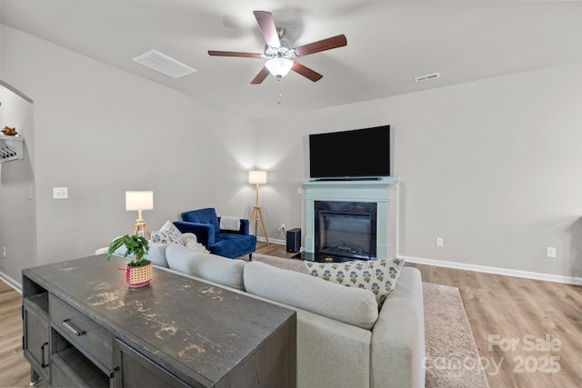 living room featuring visible vents, light wood-style floors, ceiling fan, and a glass covered fireplace