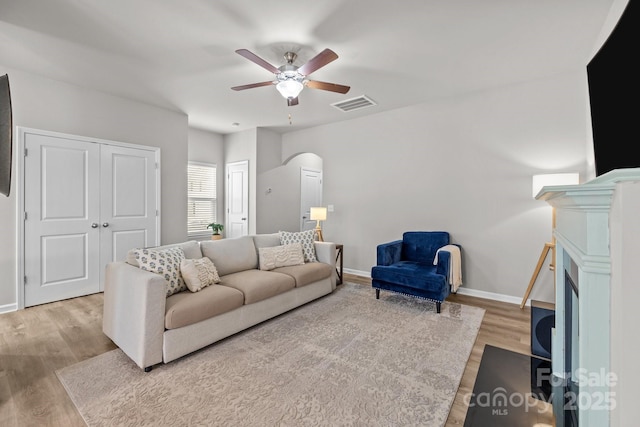 living room featuring wood finished floors, a ceiling fan, visible vents, and baseboards