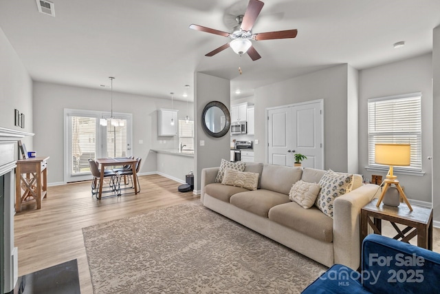 living area featuring visible vents, baseboards, ceiling fan, and wood finished floors