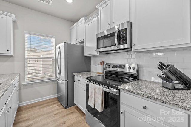 kitchen with baseboards, light wood-style flooring, stainless steel appliances, white cabinetry, and backsplash