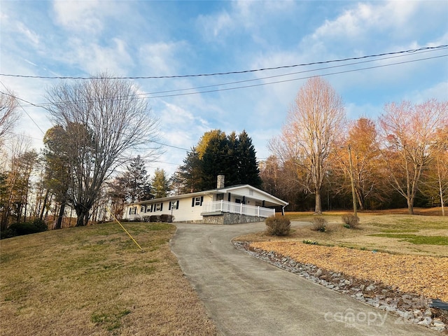 view of front of house with covered porch, driveway, a chimney, and a front lawn