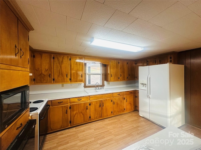 kitchen featuring white appliances, brown cabinetry, light wood-style flooring, a sink, and light countertops