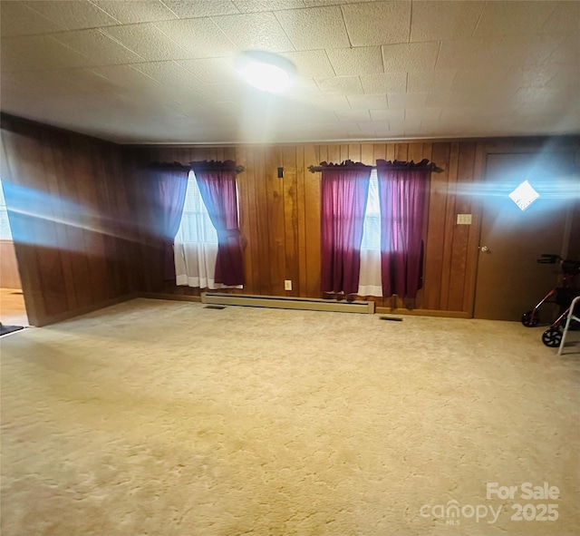 carpeted spare room featuring a baseboard heating unit and wood walls