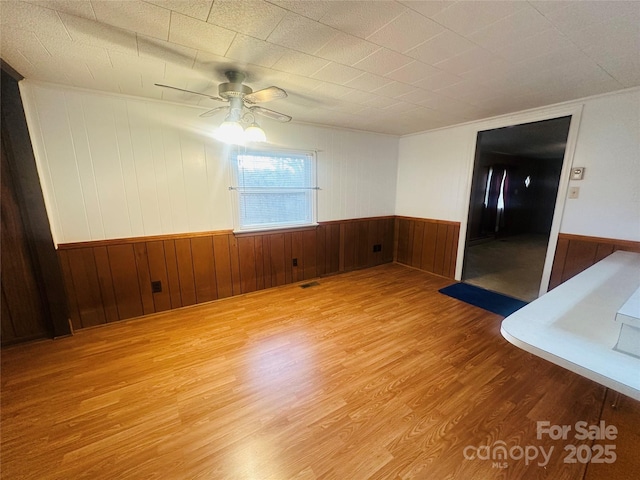 unfurnished room featuring visible vents, a ceiling fan, wood finished floors, and wainscoting