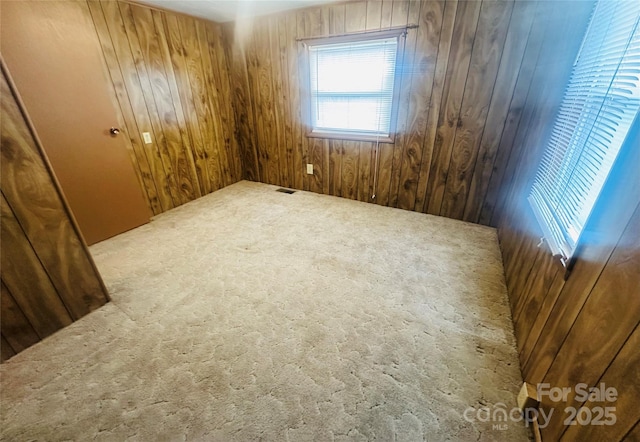 carpeted empty room featuring wooden walls and visible vents