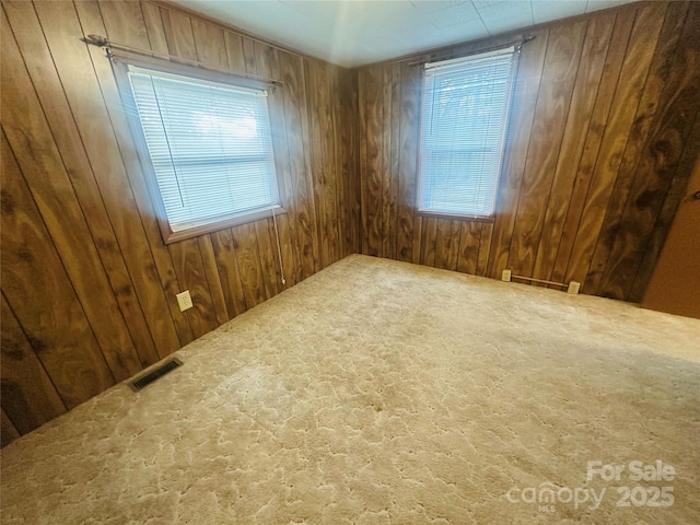 unfurnished room with wooden walls, carpet flooring, and visible vents