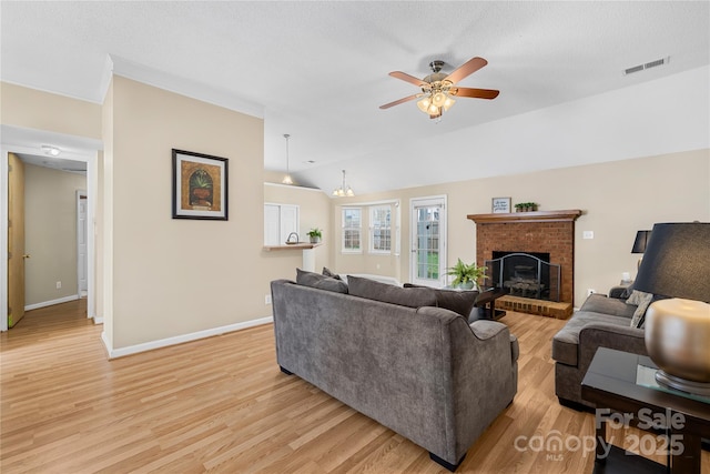 living room featuring visible vents, a fireplace, light wood finished floors, ceiling fan, and vaulted ceiling