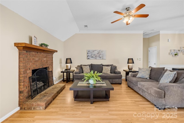 living area featuring light wood-style flooring, crown molding, lofted ceiling, a brick fireplace, and ceiling fan